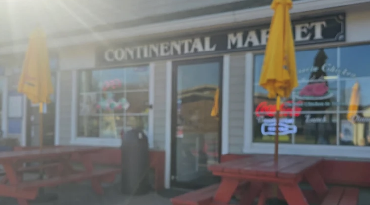 Storefront of Continental Market with red picnic tables and yellow umbrellas on S Etna Ave in Montauk